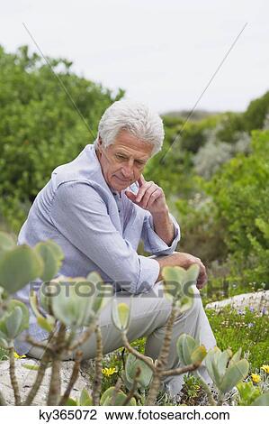 Stock Image - Senior man in a garden looking at flowers. Fotosearch