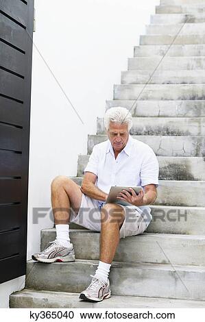 Senior man sitting on steps and using a digital tablet View Large Photo Image Stock Image - Senior man sitting on steps and using a digital tablet. Fotosearch