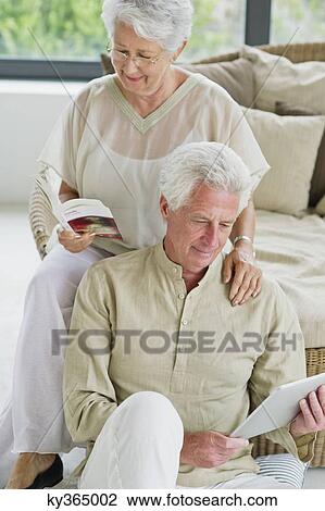 Senior man working on a digital tablet and his wife reading a magazine View Large Photo Image Stock Image - Senior man working on a digital tablet and his wife reading a magazine. Fotosearch