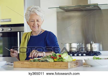 Stock Image - Senior woman cutting vegetable in a kitchen. Fotosearch