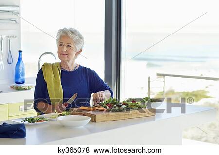 Senior woman cutting vegetable in a kitchen View Large Photo Image Stock Photo - Senior woman cutting vegetable in a kitchen. Fotosearch