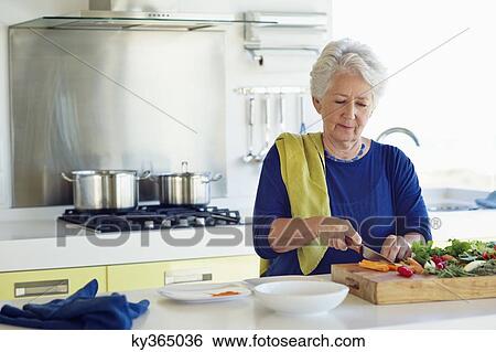 Senior woman cutting vegetable in a kitchen View Large Photo Image Stock Photograph - Senior woman cutting vegetable in a kitchen. Fotosearch