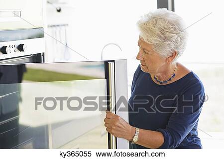 Senior woman looking into an oven View Large Photo Image Stock Photography - Senior woman looking into an oven. Fotosearch