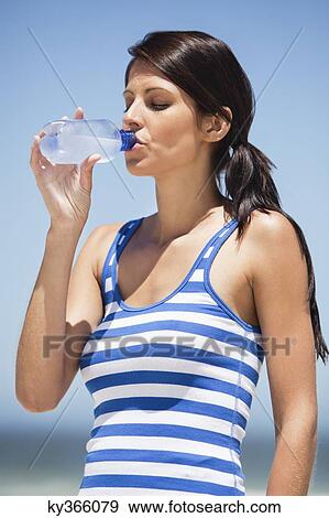 Stock Photo - Close-up of a woman drinking water from a water bottle on the beach. Fotosearch