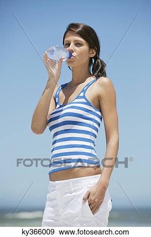 Stock Photo - Portrait of a woman drinking water from a water bottle on the beach. Fotosearch