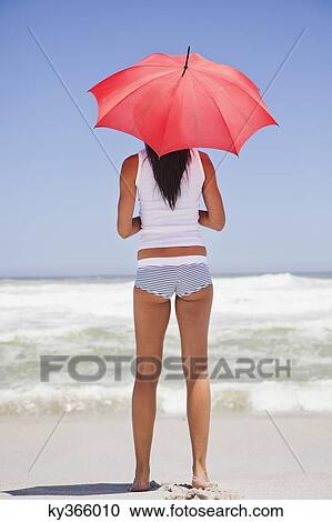Woman standing on the beach with an umbrella and looking at sea view View Large Photo Image Stock Image - Woman standing on the beach with an umbrella and looking at sea view. Fotosearch
