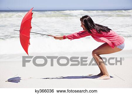 Woman trying to hold an umbrella in strong wind on the beach View Large Photo Image Stock Photograph - Woman trying to hold an umbrella in strong wind on the beach. Fotosearch