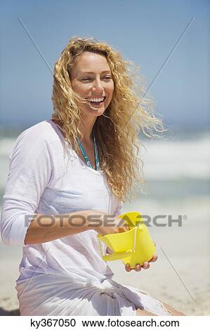 Stock Image - Beautiful woman holding plastic bucket on the beach. Fotosearch