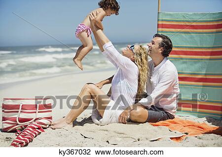 Stock Image - Couple playing with their daughter on the beach. Fotosearch