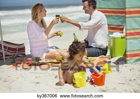 Couple toasting with drink while their daughter playing on the beach View Large Photo Image Stock Photograph - Couple toasting with drink while their daughter playing on the beach. Fotosearch