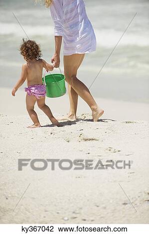 Stock Image - Low section view of a woman walking with her daughter on the beach. Fotosearch