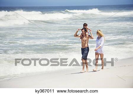 Stock Image - Man carrying his daughter on his shoulders with wife walking along with him. Fotosearch