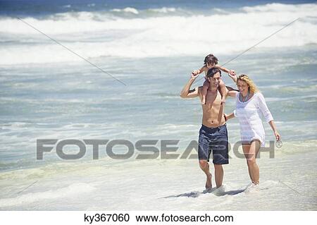 Stock Image - Man carrying his daughter on his shoulders with wife walking along with him. Fotosearch