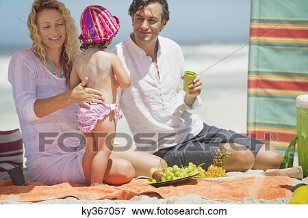 Mother applying suntan lotion to her daughter's back on the beach View Large Photo Image Stock Photo - Mother applying suntan lotion to her daughter's back on the beach. Fotosearch