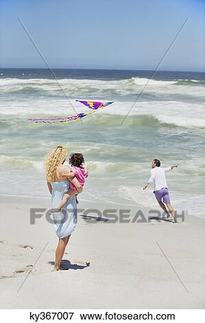 Mother carrying child while man flying kite on the beach View Large Photo Image Stock Photo - Mother carrying child while man flying kite on the beach. Fotosearch