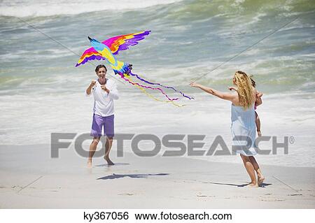 Mother carrying child while man flying kite on the beach View Large Photo Image Stock Photograph - Mother carrying child while man flying kite on the beach. Fotosearch