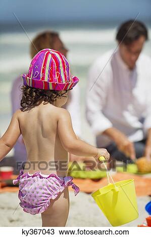 Stock Image - Rear view of a girl carrying a bucket on the beach. Fotosearch