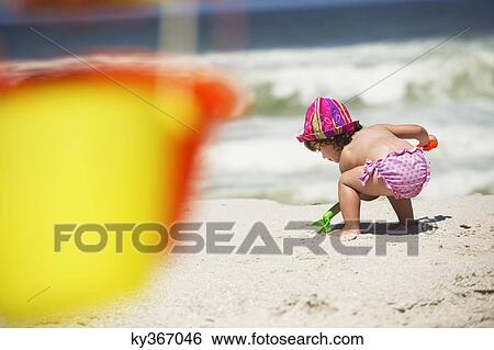 Rear view of a girl digging with a sand shovel on the beach View Large Photo Image Stock Photograph - Rear view of a girl digging with a sand shovel on the beach. Fotosearch