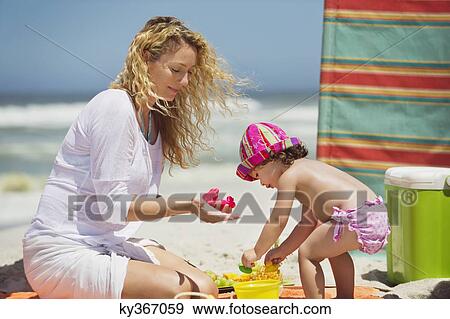 Stock Photo - Woman with her daughter playing with pail and shovel on the beach. Fotosearch