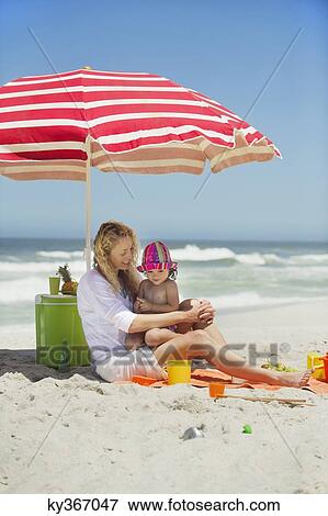 Stock Photo - Woman with her daughter sitting on the beach. Fotosearch