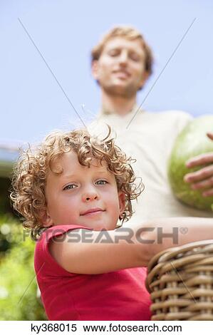 Stock Photography - Low angle view of father and son holding fruits. Fotosearch