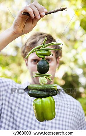 Stock Image - Man holding vegetables hanging on a twig. Fotosearch