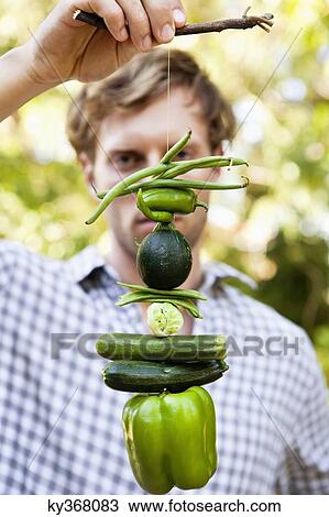 Man holding vegetables hanging on a twig View Large Photo Image Stock Image - Man holding vegetables hanging on a twig. Fotosearch