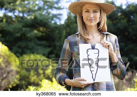 Stock Photography - Portrait of a young woman showing carrot painting in a field. Fotosearch