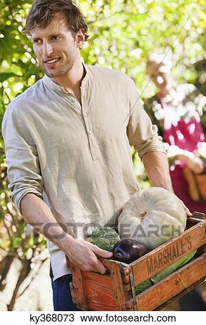 Stock Image - Smiling man holding a crate of vegetables. Fotosearch