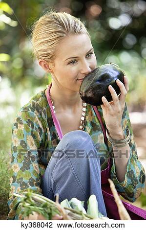 Stock Image - Smiling woman smelling eggplant. Fotosearch