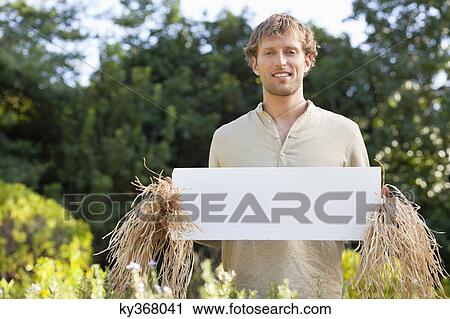Young man in scarecrow dressing and holding a blank placard in a field View Large Photo Image Stock Image - Young man in scarecrow dressing and holding a blank placard in a field. Fotosearch