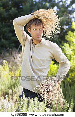 Stock Photography - Young man standing in a field as scarecrow. Fotosearch