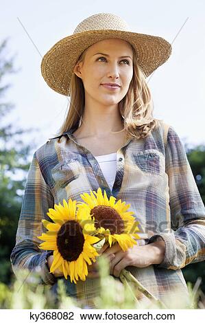 Young woman holding sunflowers in a field View Large Photo Image Stock Image - Young woman holding sunflowers in a field. Fotosearch