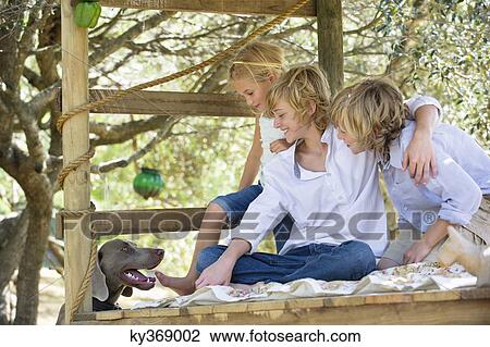 Stock Image - Children looking at a dog from tree house. Fotosearch