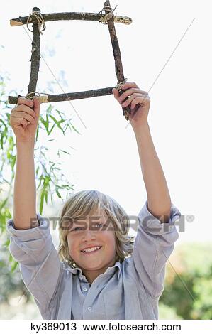 Portrait of a cute little boy holding frame of driftwood with arms raised outdoors View Large Photo Image Stock Image - Portrait of a cute little boy holding frame of driftwood with arms raised outdoors. Fotosearch