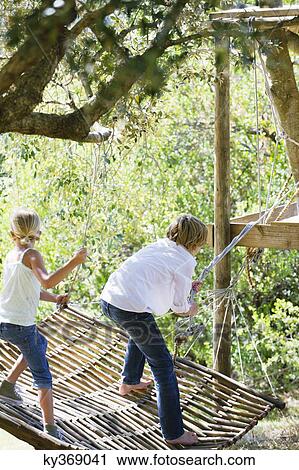 Stock Image - Rear view of siblings tying hammock to tree. Fotosearch