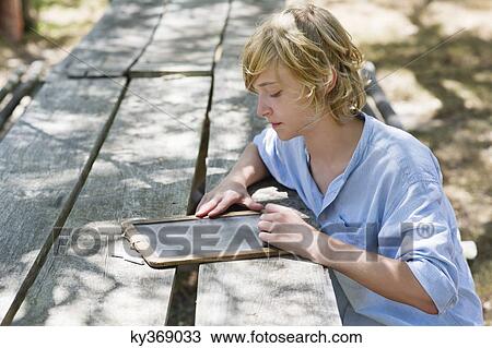 Stock Image - Side profile of a little boy writing on slate outdoors. Fotosearch