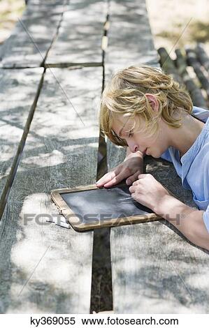 Side profile of a little boy writing on slate outdoors View Large Photo Image Stock Photography - Side profile of a little boy writing on slate outdoors. Fotosearch