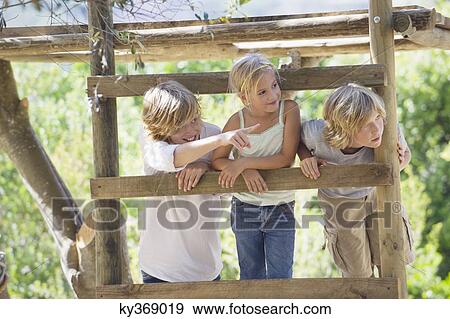 Stock Photo - Smiling children looking away from tree house. Fotosearch