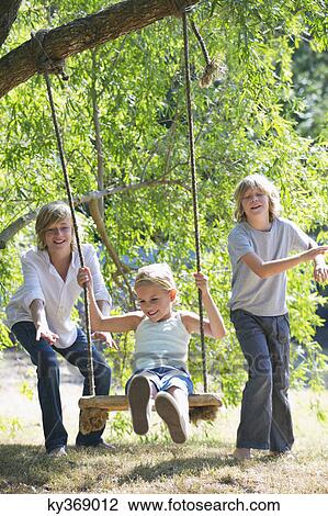 Stock Image - Smiling little siblings playing in tree swing. Fotosearch