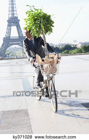 Stock Photo - Businessman carrying a plant on a bicycle with the Eiffel Tower in the background, Paris, Ile-de-France, France. Fotosearch