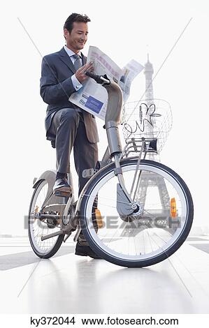 Businessman reading a newspaper on a bicycle with the Eiffel Tower in the background, Paris, Ile-de-France, France View Large Photo Image Picture - Businessman reading a newspaper on a bicycle with the Eiffel Tower in the background, Paris, Ile-de-France, France. Fotosearch