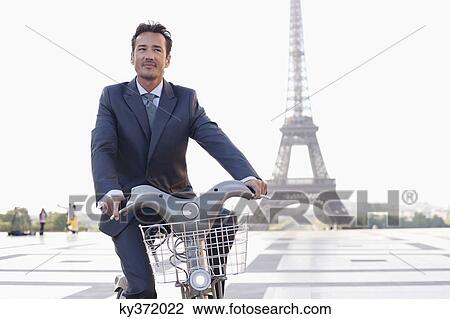 Stock Image - Businessman riding a bicycle with the Eiffel Tower in the background, Paris, Ile-de-France, France. Fotosearch