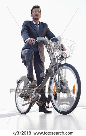 Stock Photo - Businessman riding a bicycle with the Eiffel Tower in the background, Paris, Ile-de-France, France. Fotosearch