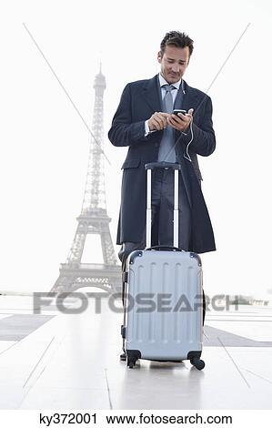 Businessman standing with luggage using a mobile phone with the Eiffel Tower in the background, Paris, Ile-de-France, France View Large Photo Image Stock Image - Businessman standing with luggage using a mobile phone with the Eiffel Tower in the background, Paris, Ile-de-France, France. Fotosearch