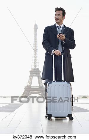 Stock Photo - Businessman standing with luggage with the Eiffel Tower in the background, Paris, Ile-de-France, France. Fotosearch