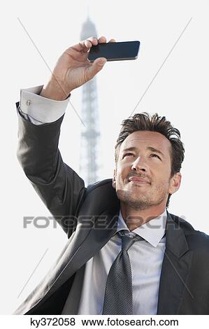 Stock Photo - Businessman taking a picture of himself with the Eiffel Tower in the background, Paris, Ile-de-France, France. Fotosearch