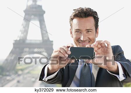 Businessman taking a picture with a mobile phone with the Eiffel Tower in the background, Paris, Ile-de-France, France View Large Photo Image Stock Photo - Businessman taking a picture with a mobile phone with the Eiffel Tower in the background, Paris, Ile-de-France, France. Fotosearch