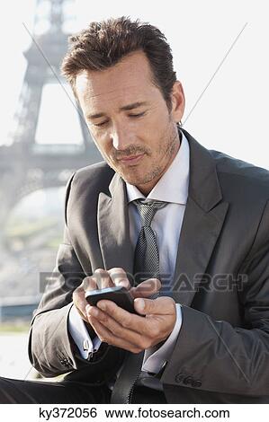 Stock Photograph - Businessman using a mobile phone with the Eiffel Tower in the background, Paris, Ile-de-France, France. Fotosearch