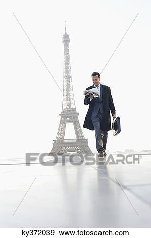 Stock Photo - Businessman walking with briefcase reading newspaper with the Eiffel Tower in the background, Paris, Ile-de-France, France. Fotosearch